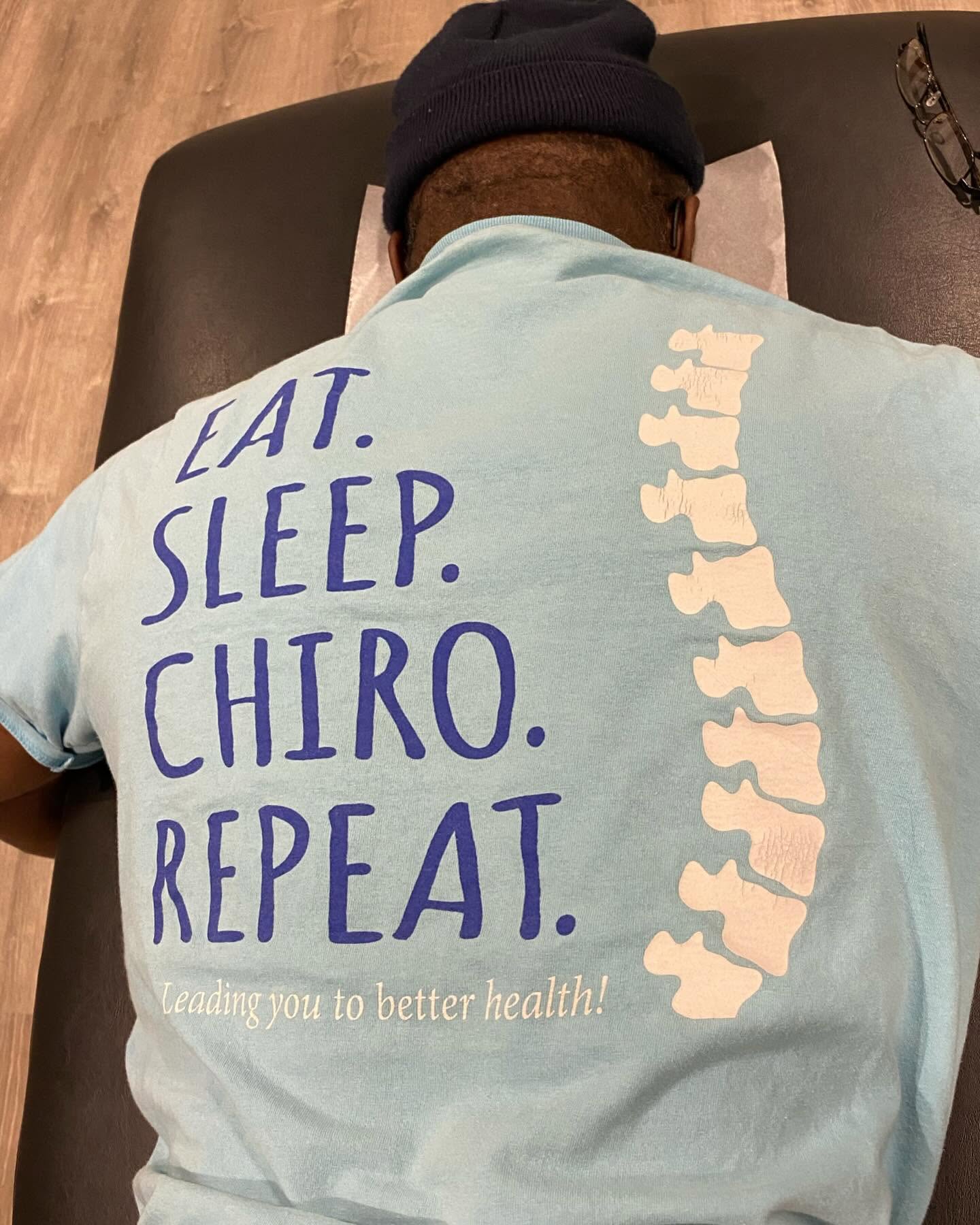 A patient in an 'Eat. Sleep. Chiro. Repeat.' shirt on the adjusting table